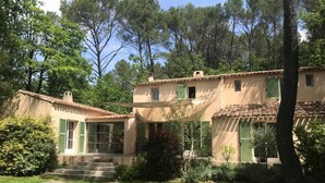 Une maison à deux étages, avec un toit recouvert de tuiles, des volets verts et un petit jardin à l’avant, accessible par quelques marches menant à l’entrée.