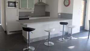 Una cocina moderna con una isla central, tres taburetes de bar y un reloj en la pared.