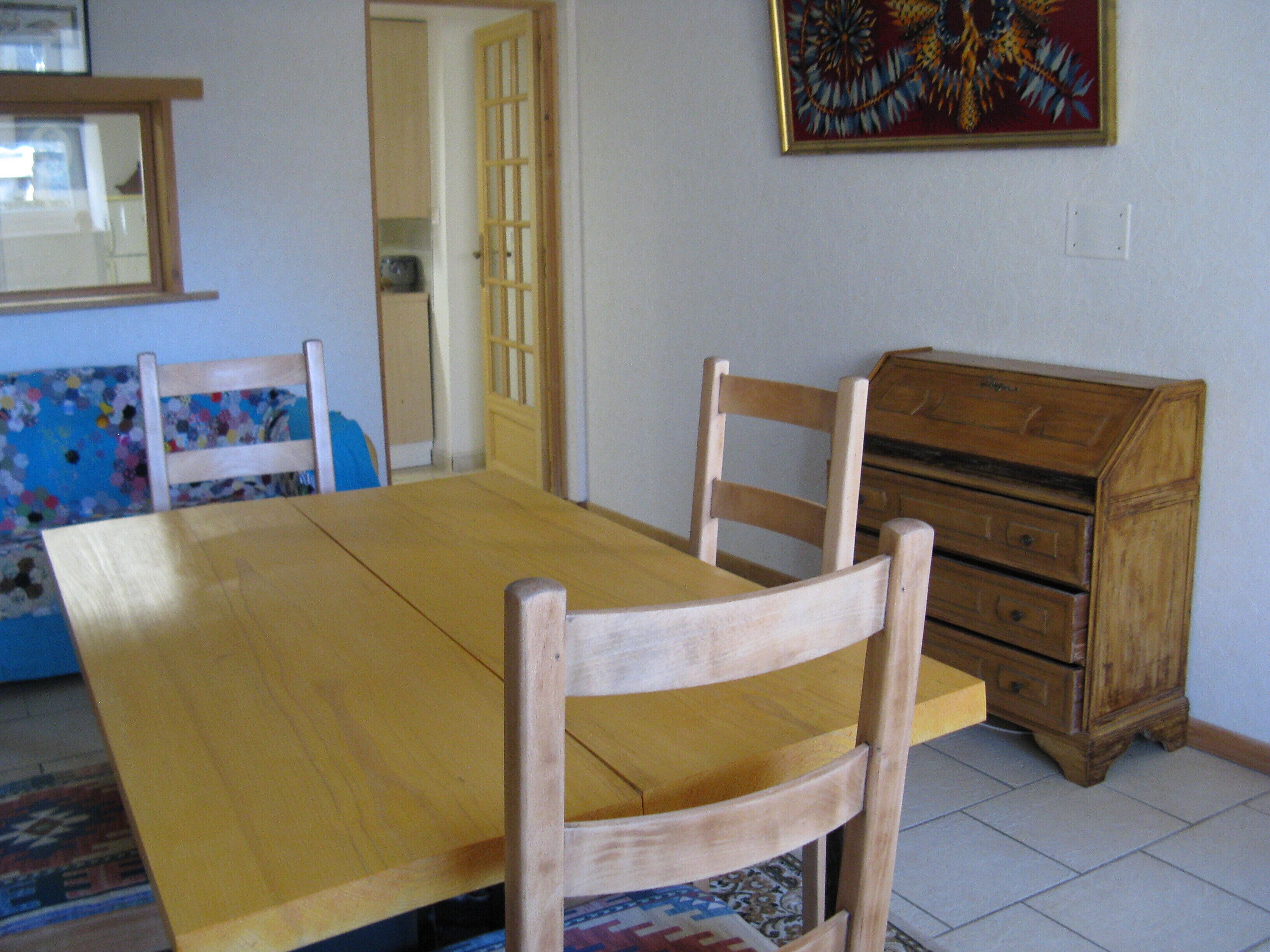 A dining area with a wooden table and chairs, a dresser, and a colorful wall hanging.