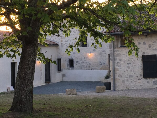 A stone building with a courtyard, a tree in the foreground, and a tiled roof. - Charming family home with swimming pool in peaceful Gascony (Nérac)