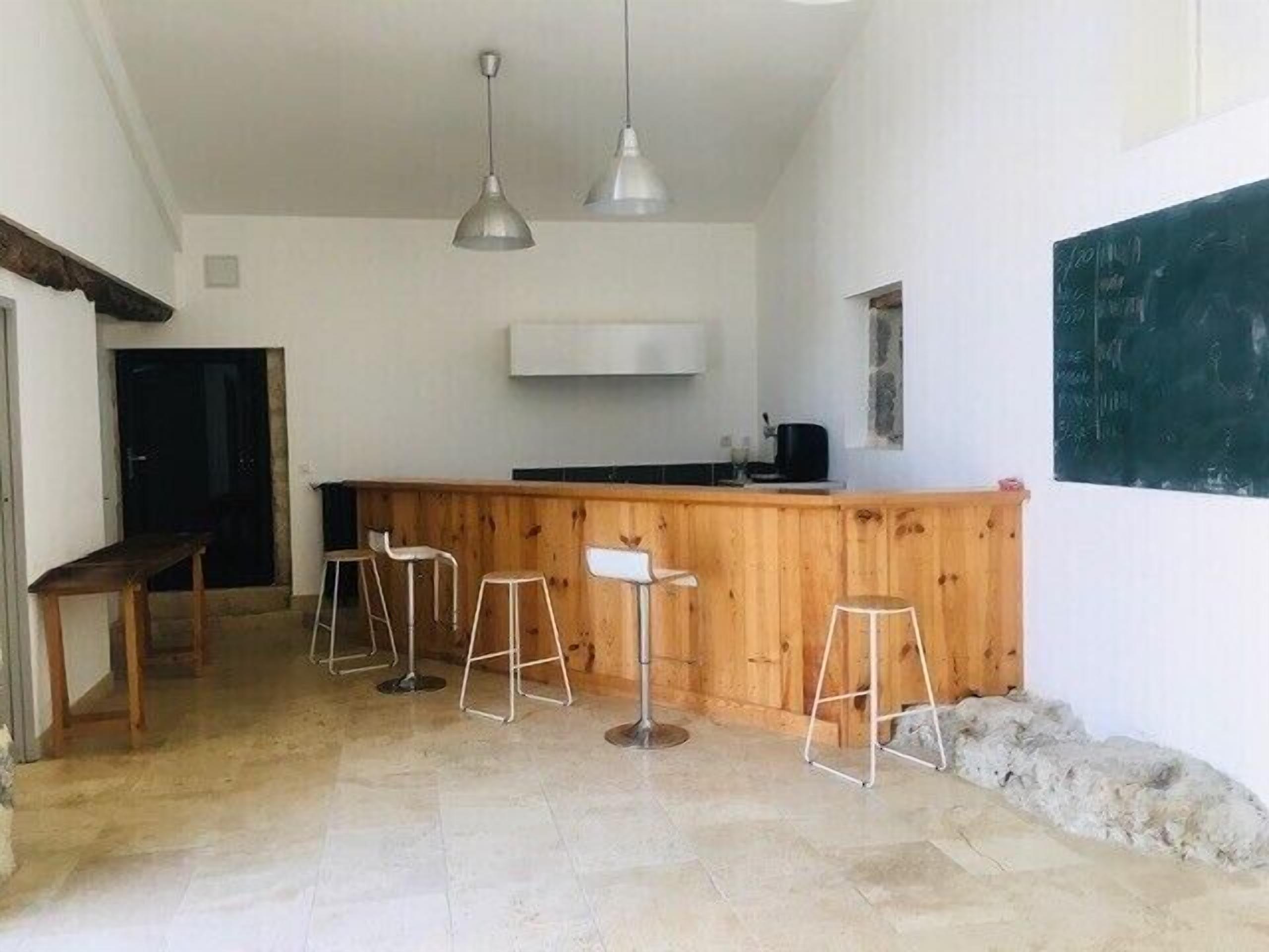 Una cocina con mostrador de madera, taburetes de bar, luces colgantes y una pizarra en la pared.