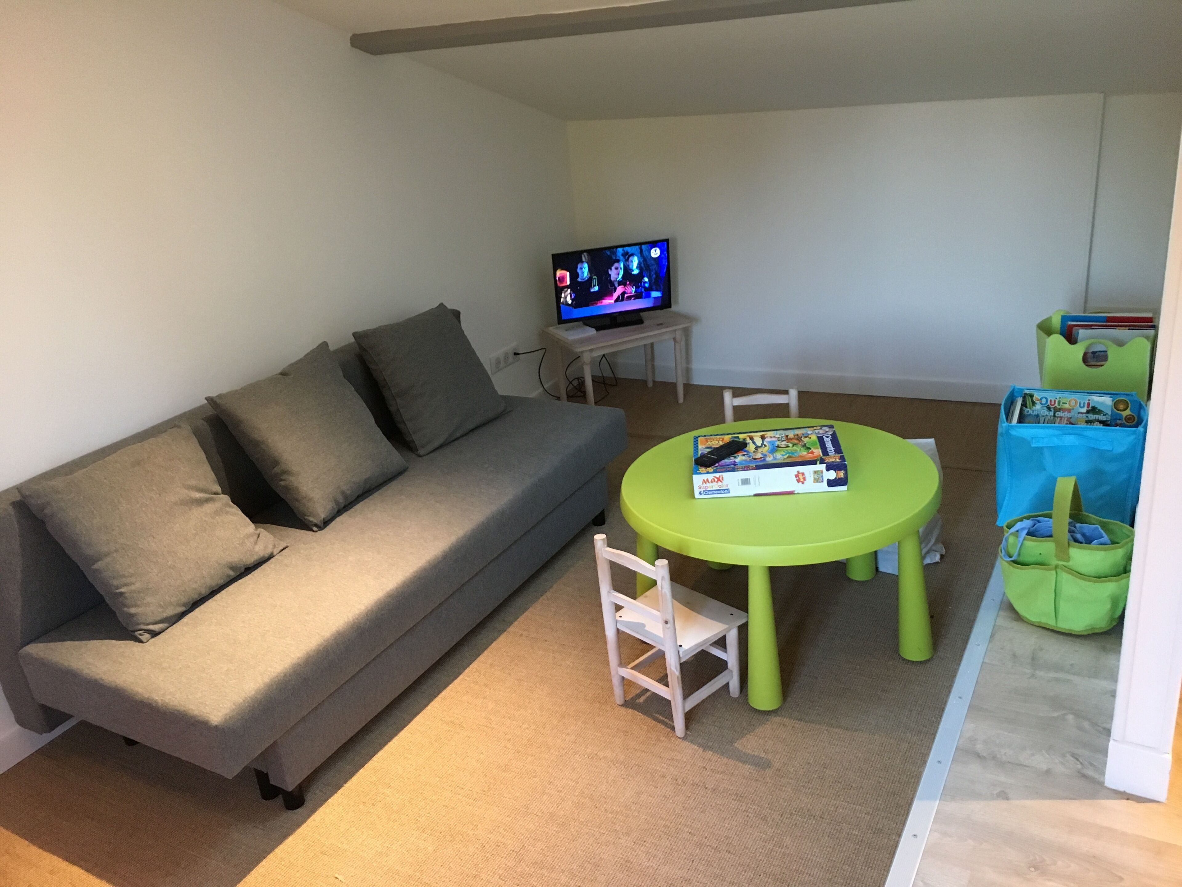 Een woonkamer met een grijze bank, een groene tafel en een televisie.