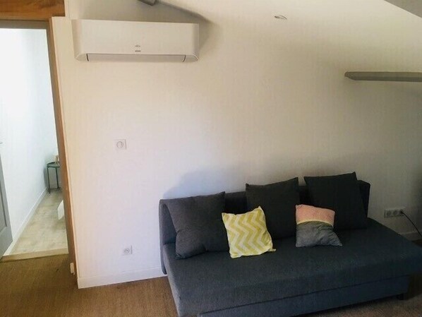 Een moderne woonkamer met een donkergrijze bank, een klein bijzettafeltje en een wandairconditioning.