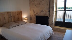A bedroom with a wooden headboard, a bed with white linens, a nightstand with a lamp, a radiator, and a window with a view of a building. - Charming family home with swimming pool in peaceful Gascony (Nérac)