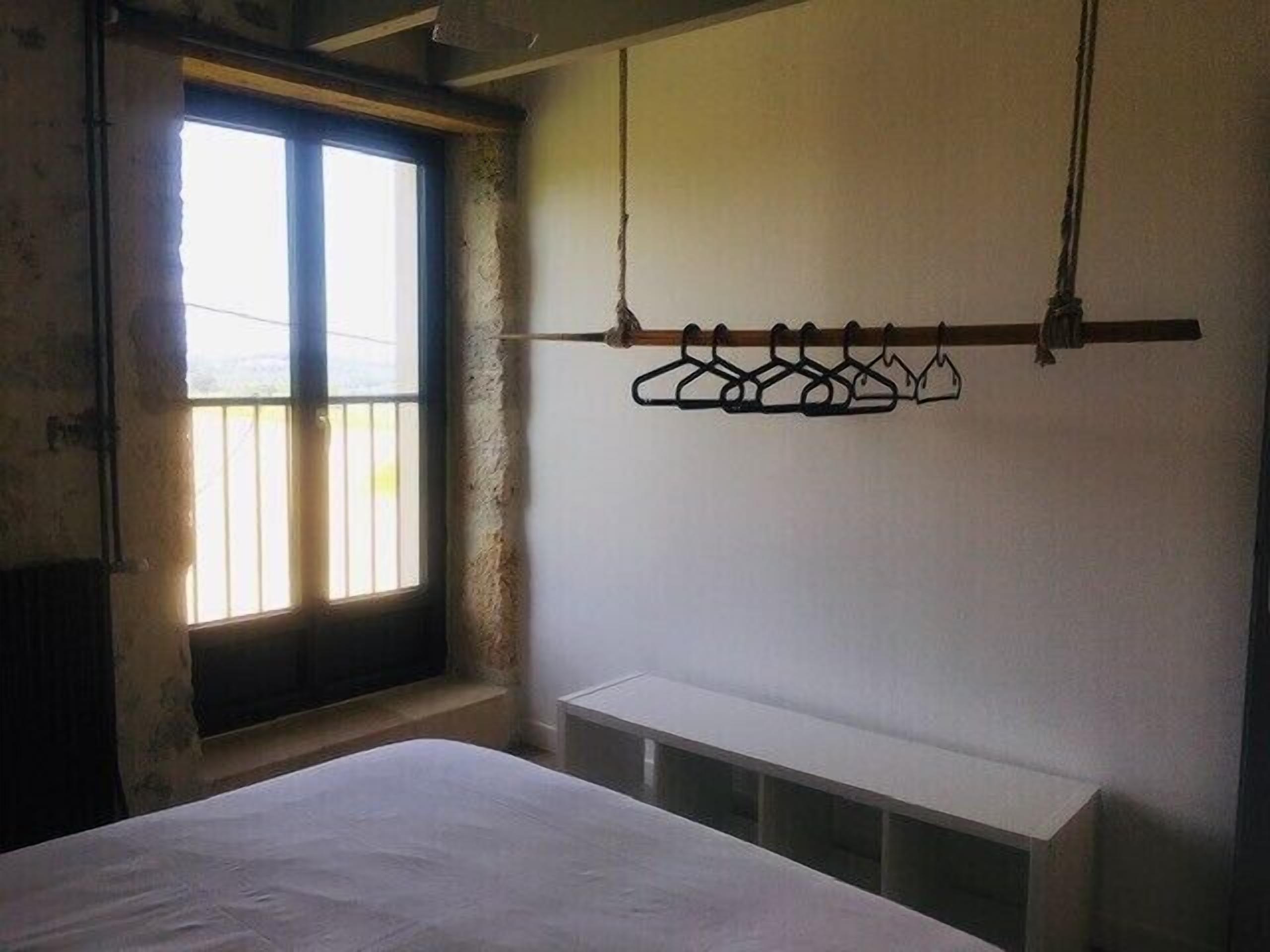 A room with a bed, a window with bars, and a wall-mounted rack with hangers.