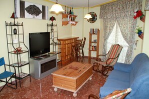 A living room with a television, wooden coffee table, blue sofa, and a dining area with chairs and a table.