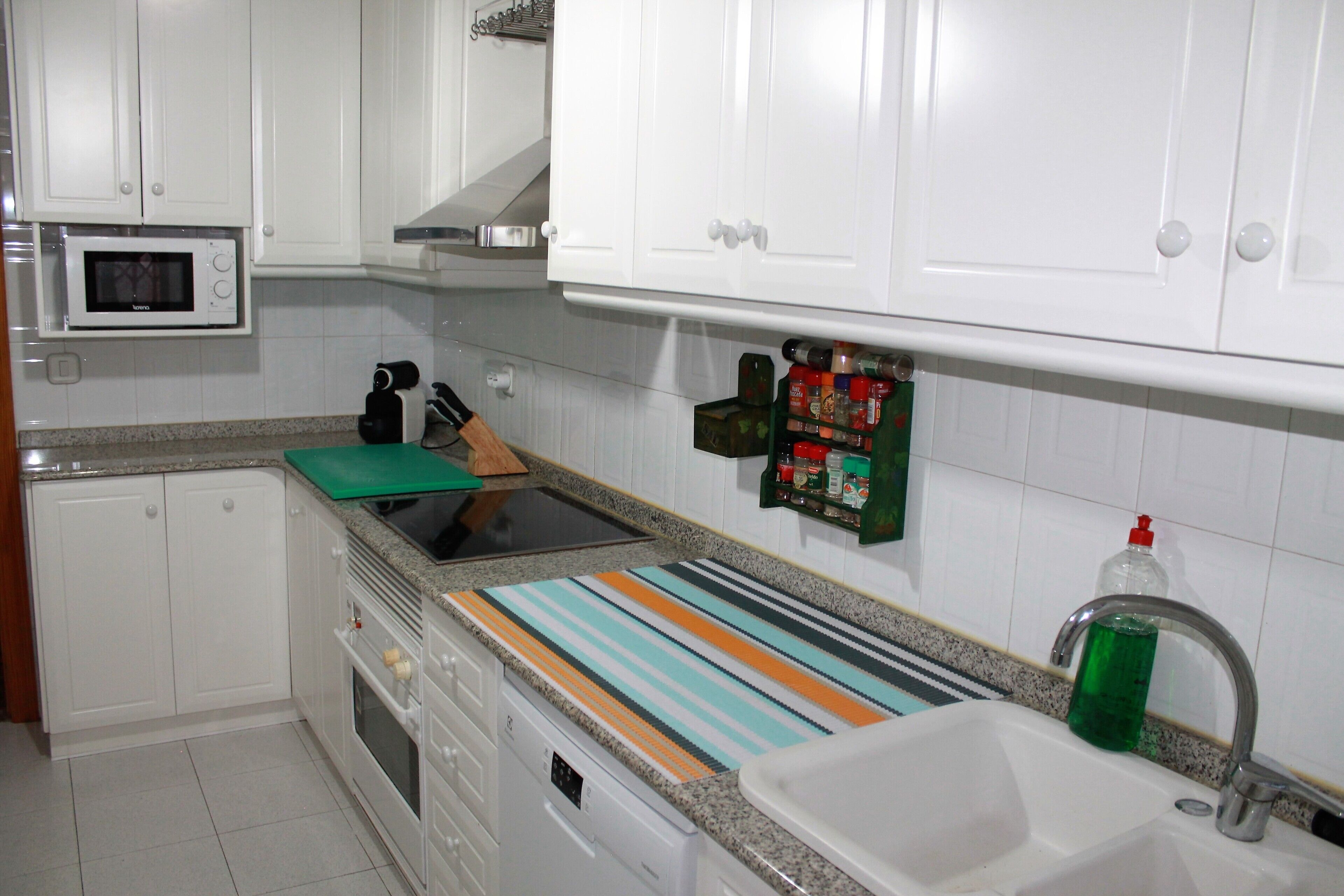 Una cocina con armarios blancos, un microondas, una estufa, un lavamanos y una tabla de cortar a rayas.