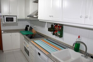 A kitchen with white cabinets, a microwave, a stove, a sink, and a striped cutting board.