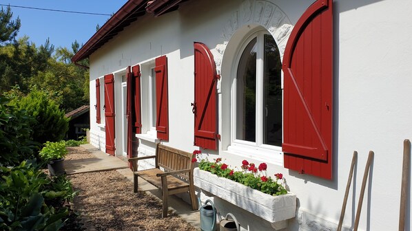 A white building with red shutters and a bench outside.