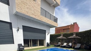 A swimming pool with a clear blue surface, surrounded by a modern building with large windows and a covered garage. - Superb villa with private heated swimming pool and gym. (Marrakech)