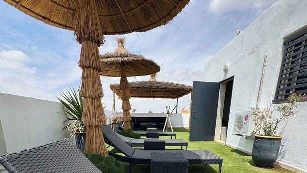 A rooftop lounge area with two lounge chairs, a large umbrella, and a small table. - Superb villa with private heated swimming pool and gym. (Marrakech)