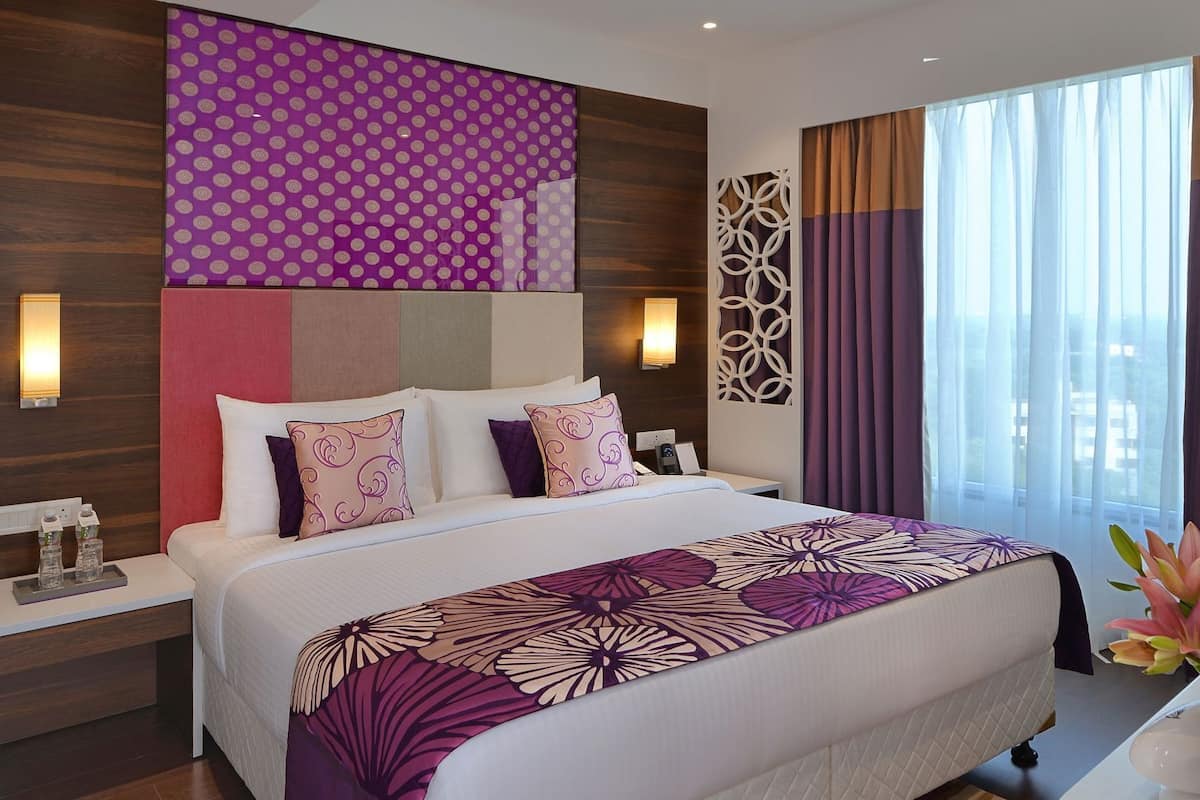 A modern hotel room with a large bed, a nightstand, a wall-mounted lamp, and a window with curtains.