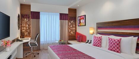 A hotel room with a bed, desk, chair, and a TV.