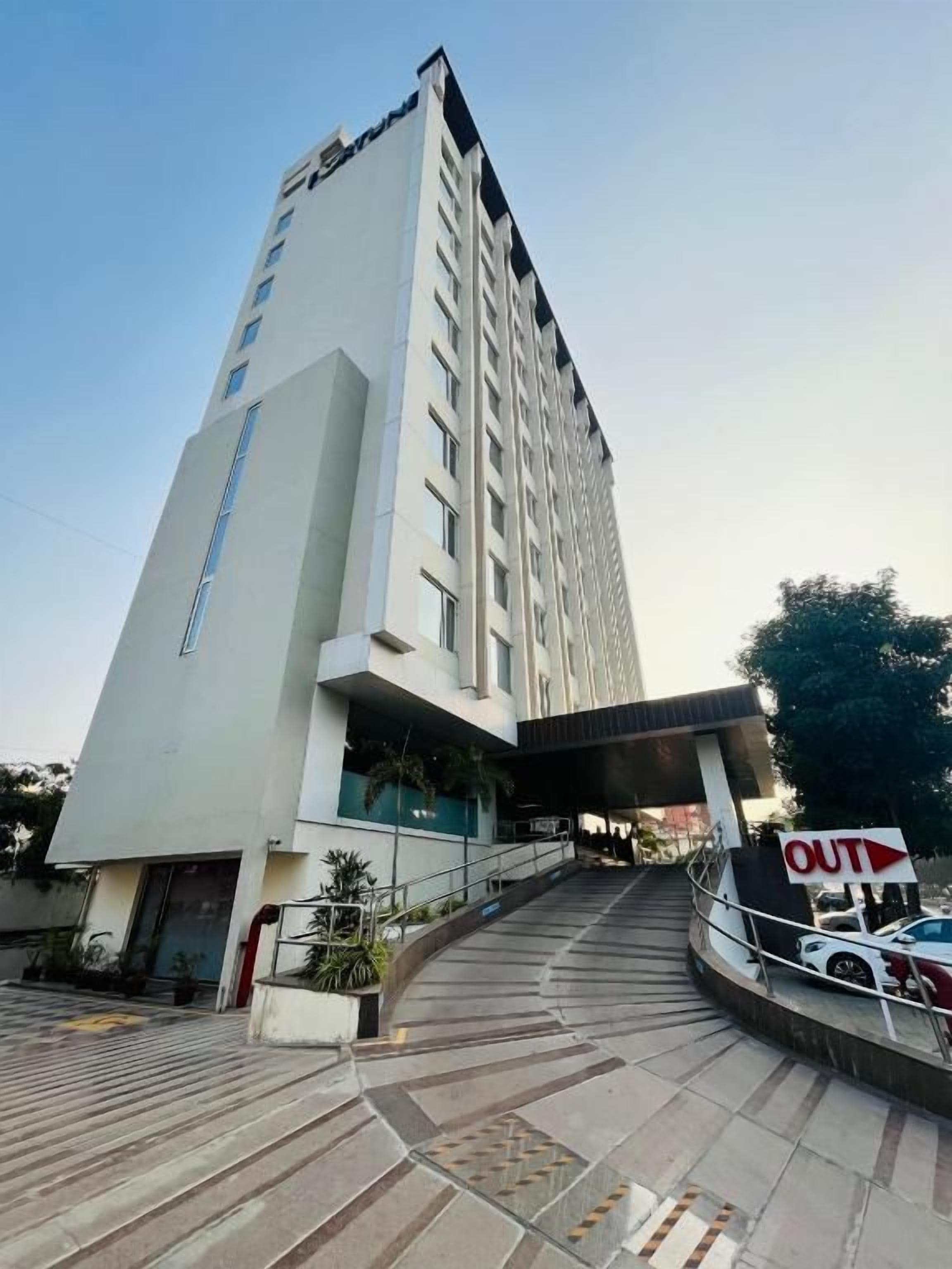 A modern hotel entrance with a staircase leading to the main building, a clear sky, and a sign indicating the exit.