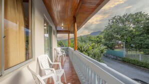 Un balcon avec des chaises en plastique blanches, un plafond en bois et une vue sur la verdure et les montagnes.