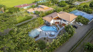 Une grande maison avec une piscine, entourée d’une végétation luxuriante et de palmiers.