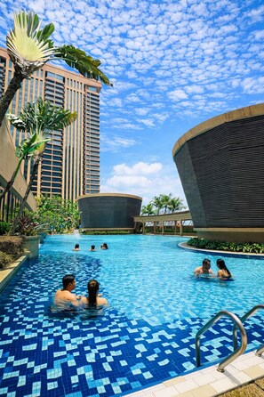A swimming pool with tiled flooring, surrounded by palm trees and modern buildings. - KL Service Apartment at Times Square (Kuala Lumpur)