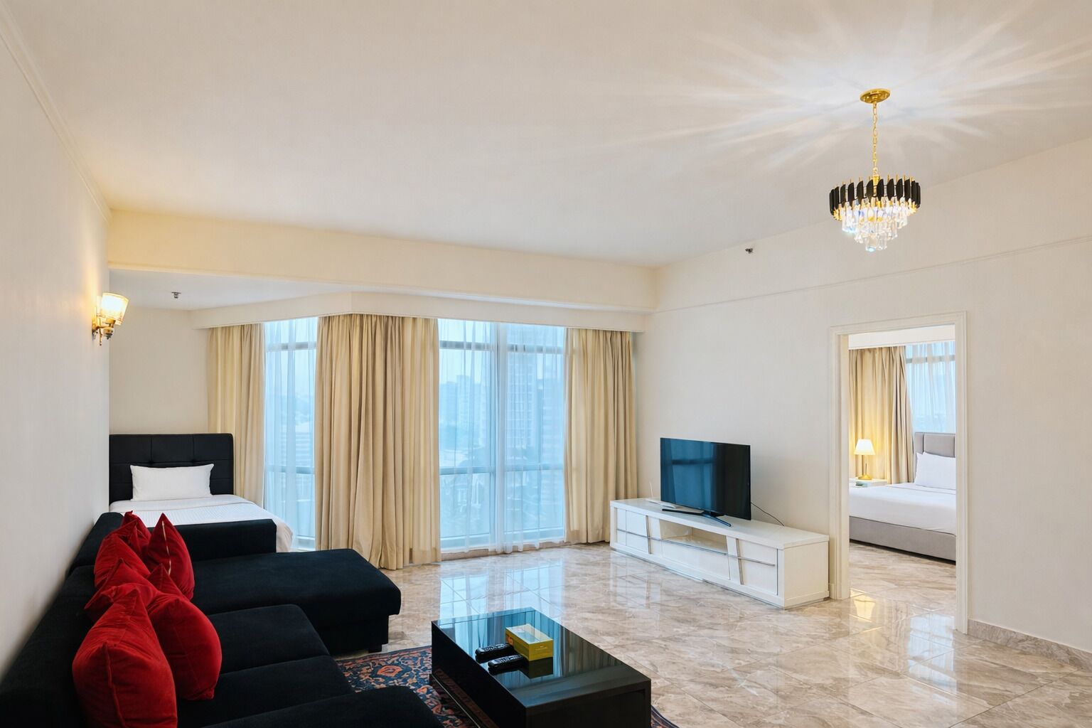 A hotel room with a bed, a TV, a coffee table, and a view of the city through large windows.