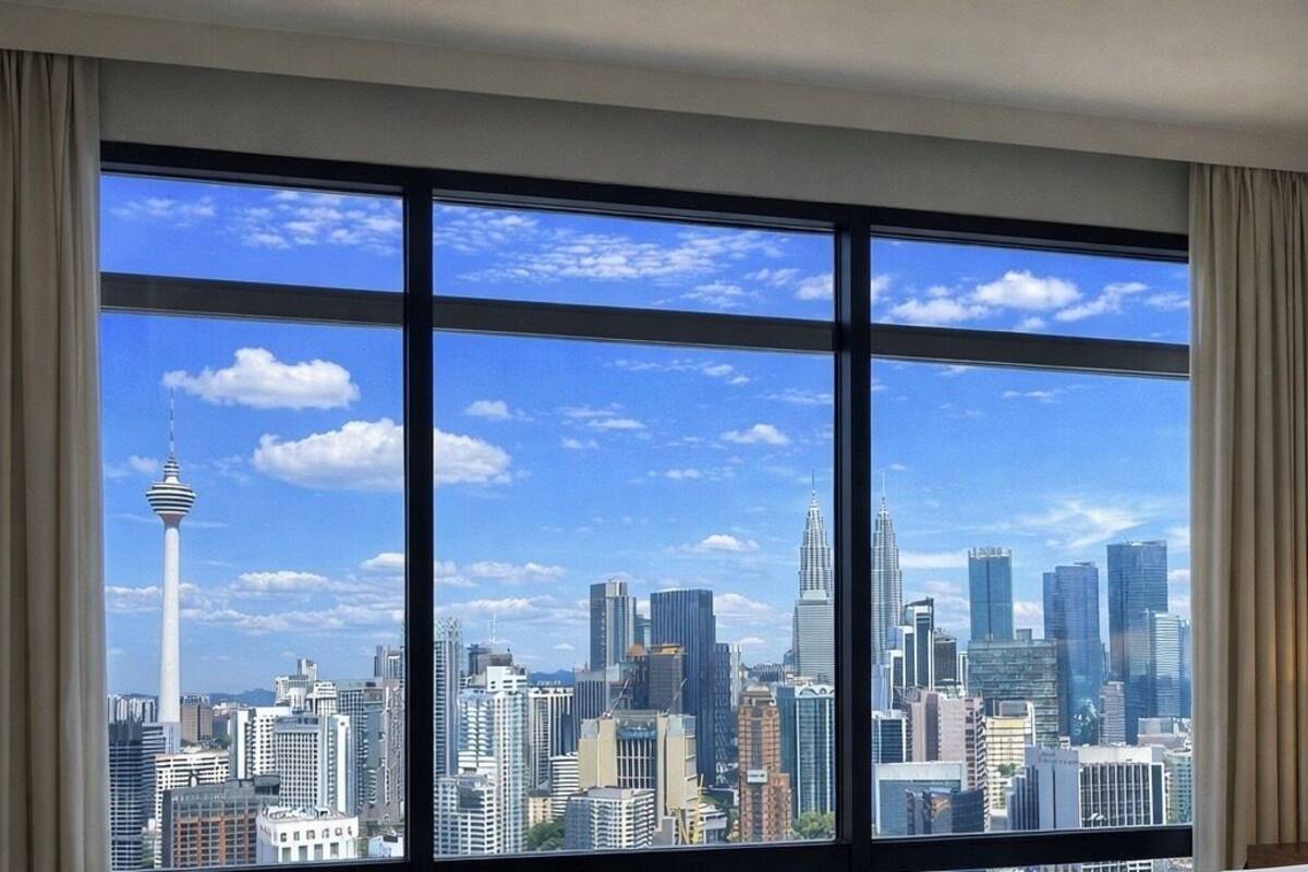 A hotel room with a large window offering a city skyline view, a bed, and a nightstand with a lamp.