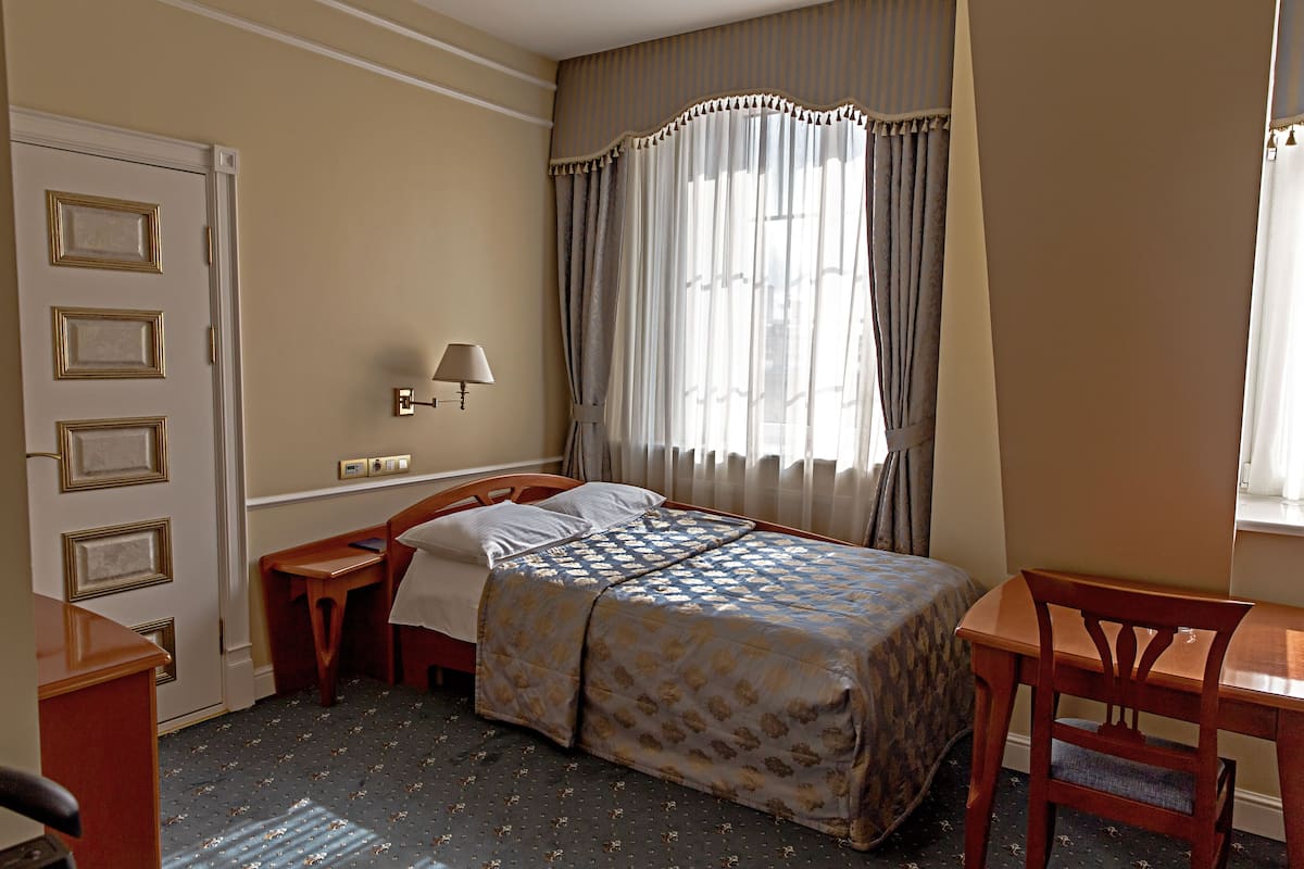 A hotel room with a bed, a desk, a chair, a lamp, and a window with curtains.