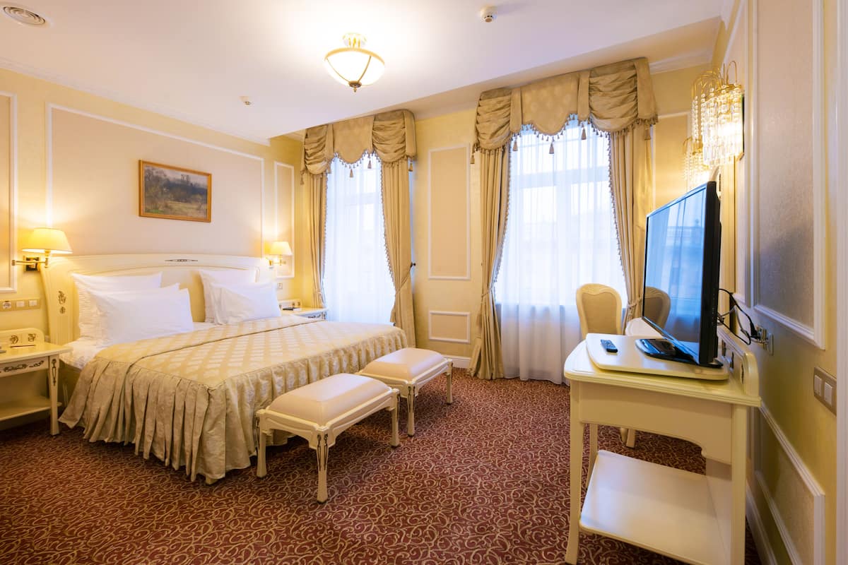 A hotel room with a large bed, a desk with a computer, a chair, and two bedside tables with lamps.