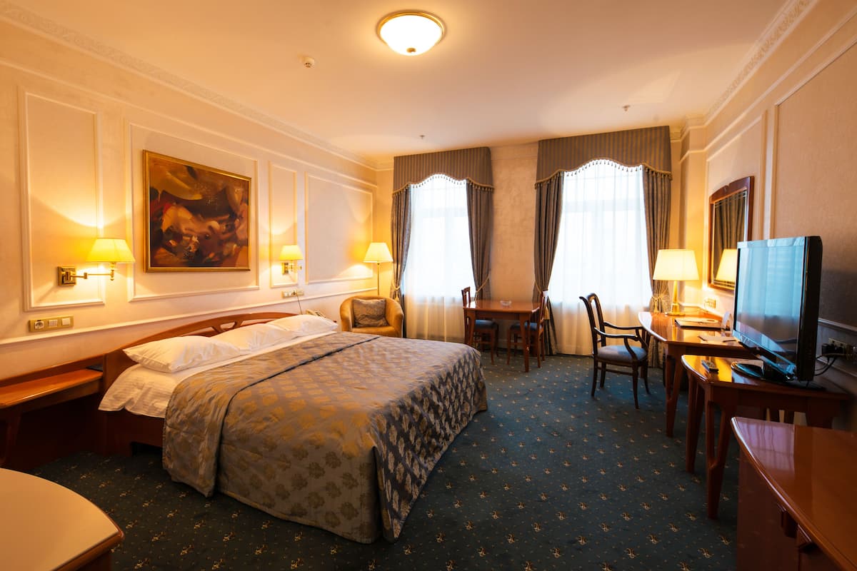 A hotel room with a large bed, a desk with a computer, a chair, and a television.