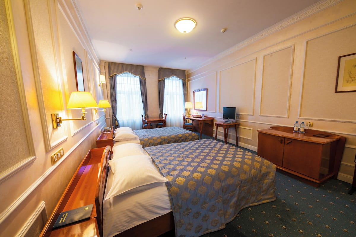 A hotel room with two beds, a desk, a chair, a small table, a mirror, and a cabinet.