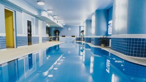 A swimming pool with blue tiled walls and a white floor, surrounded by a reception area with a counter and chairs.