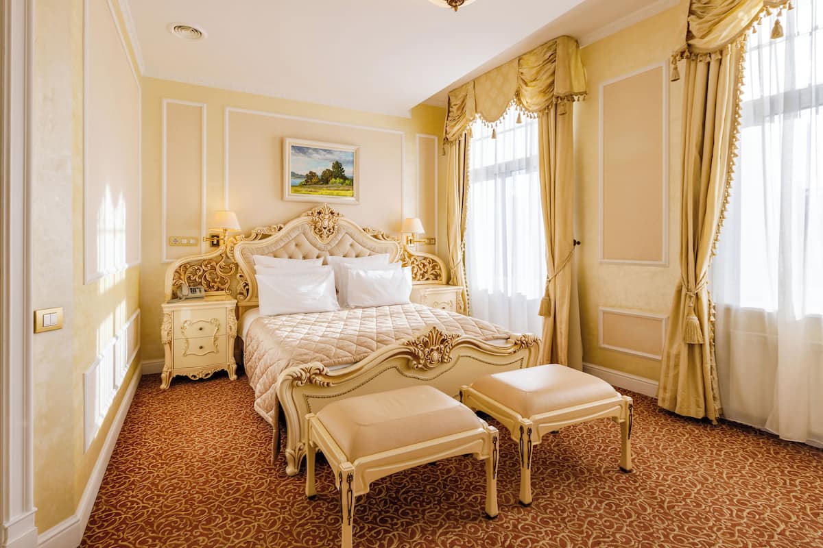 A luxurious bedroom with a large bed, two bedside tables, a nightstand, and a bench.
