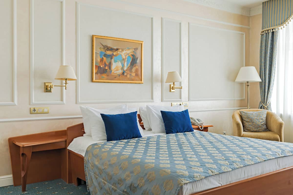 A hotel room with a large bed, two bedside tables, a chair, and a painting on the wall.