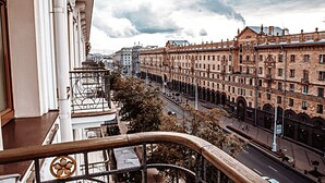 A balcony with a wrought iron railing overlooking a city street lined with historic buildings.