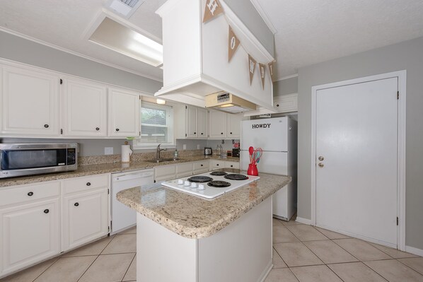 A kitchen with white cabinets, a granite countertop, a built-in microwave, a stove, and a refrigerator.