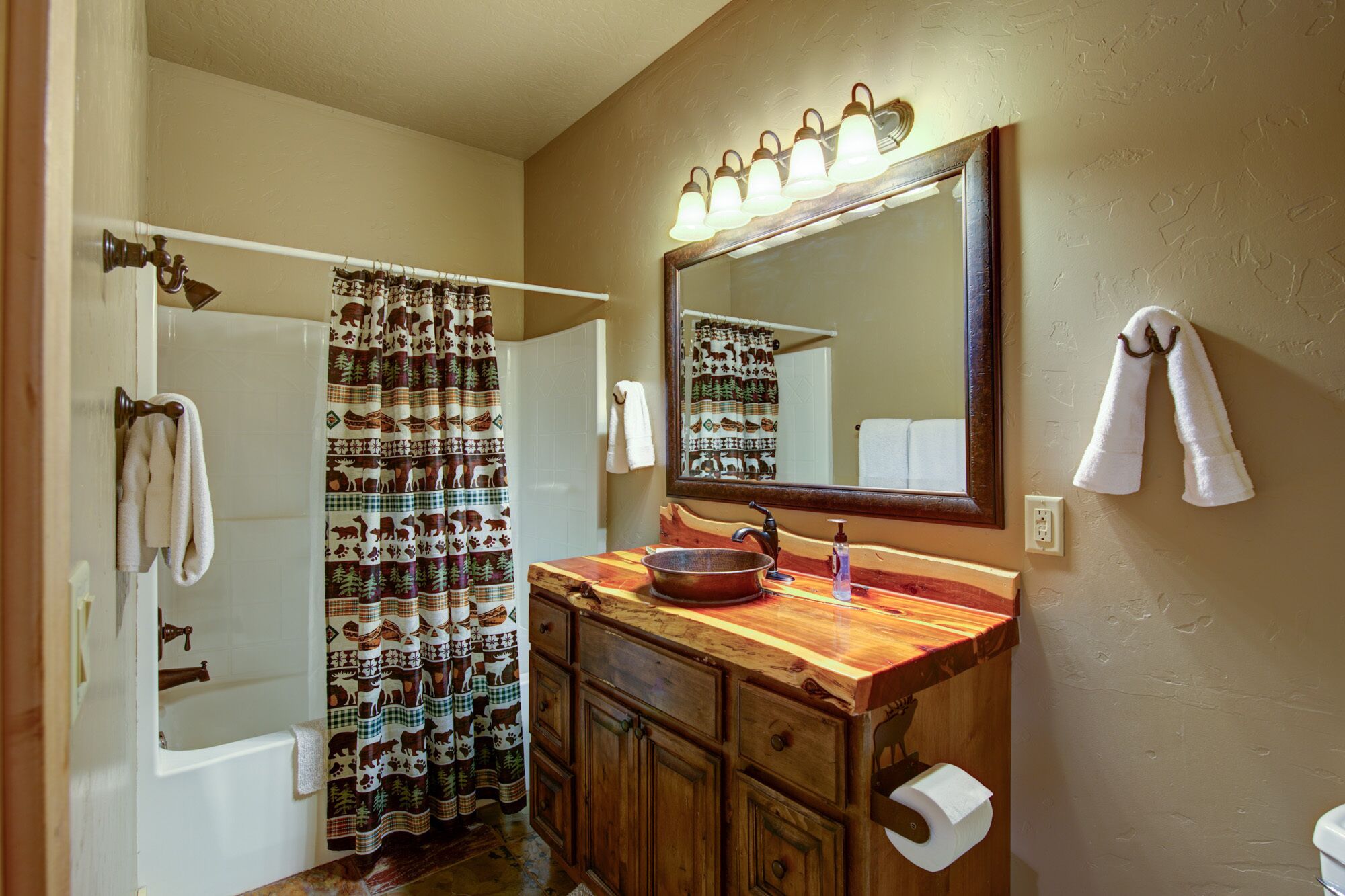 A bathroom with a wooden vanity, a large mirror, a shower curtain with animal prints, and a towel rack.