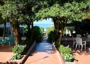 Relax in a shaded outdoor space with a clear sea view, featuring a paved patio, comfortable seating, and a dining table.