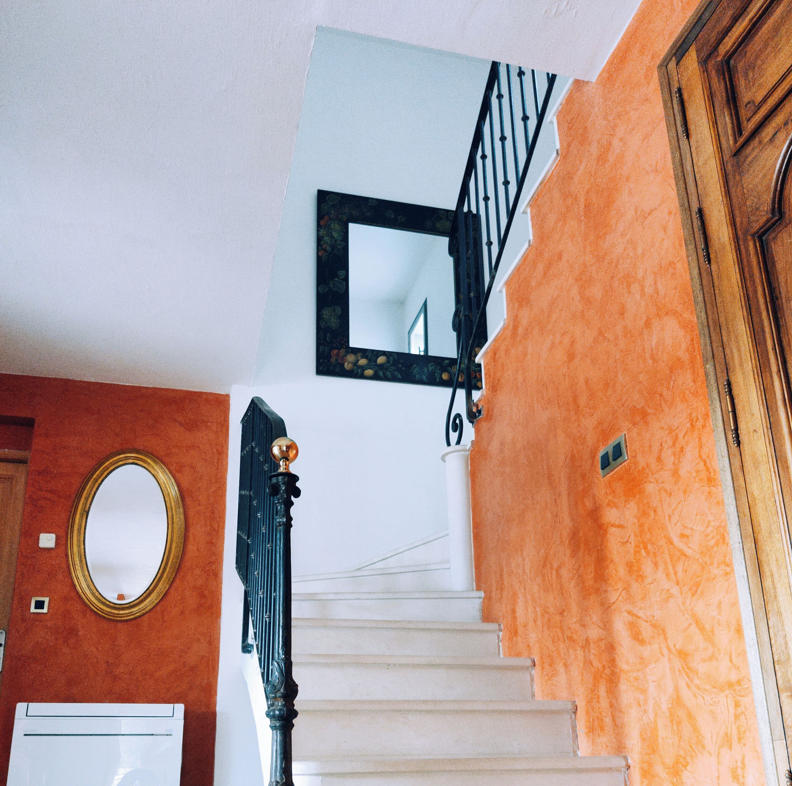 Un escalier aux marches blanches menant à un palier, une balustrade noire et un miroir accroché au mur.