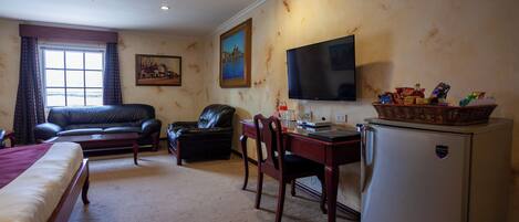 A hotel room with a bed, a desk, a chair, a television, and a refrigerator.