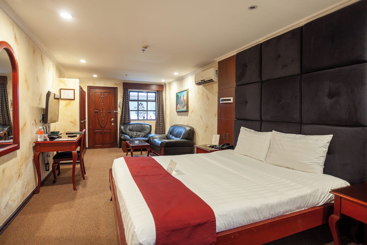 Une chambre d’hôtel avec un grand lit, un bureau, une chaise, une armoire et une fenêtre avec des rideaux.