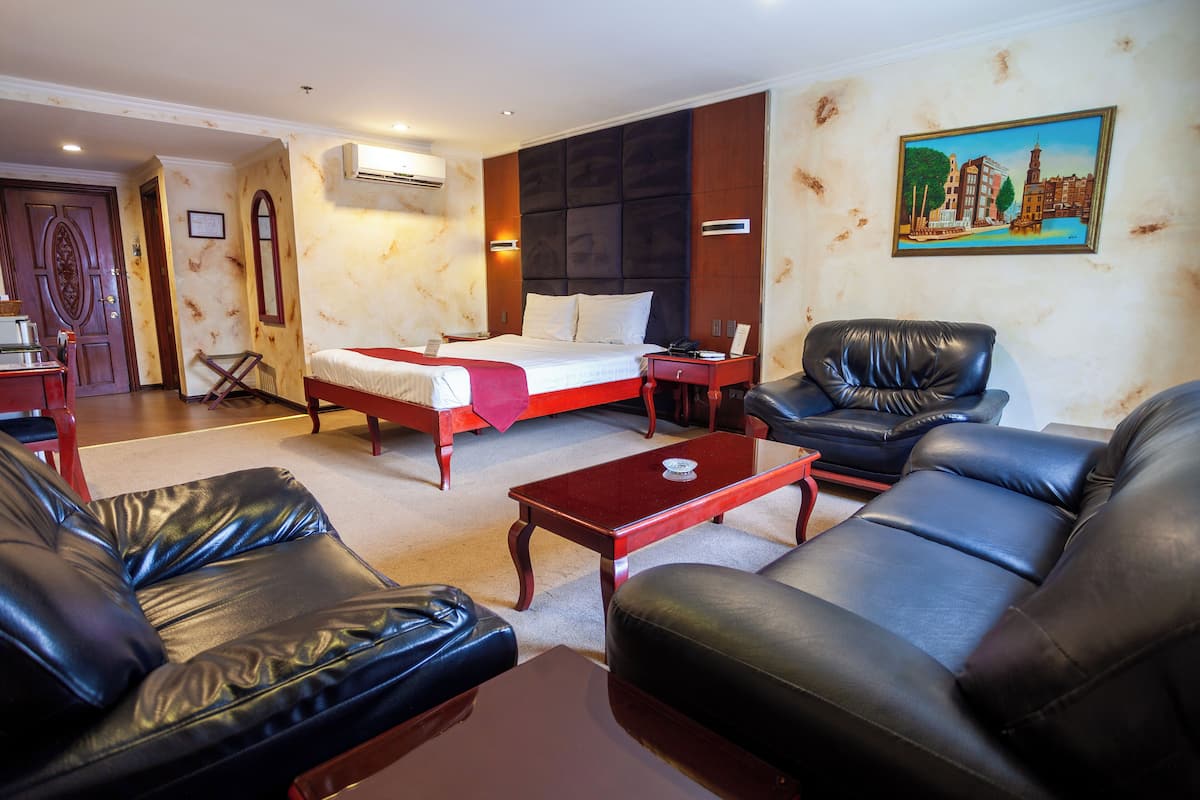 Une chambre d’hôtel avec un lit, deux canapés en cuir, une table basse, un bureau et un tableau au mur.