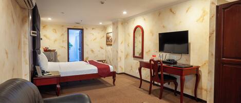 A hotel room with a bed, a desk with a chair, a TV, and a couch.