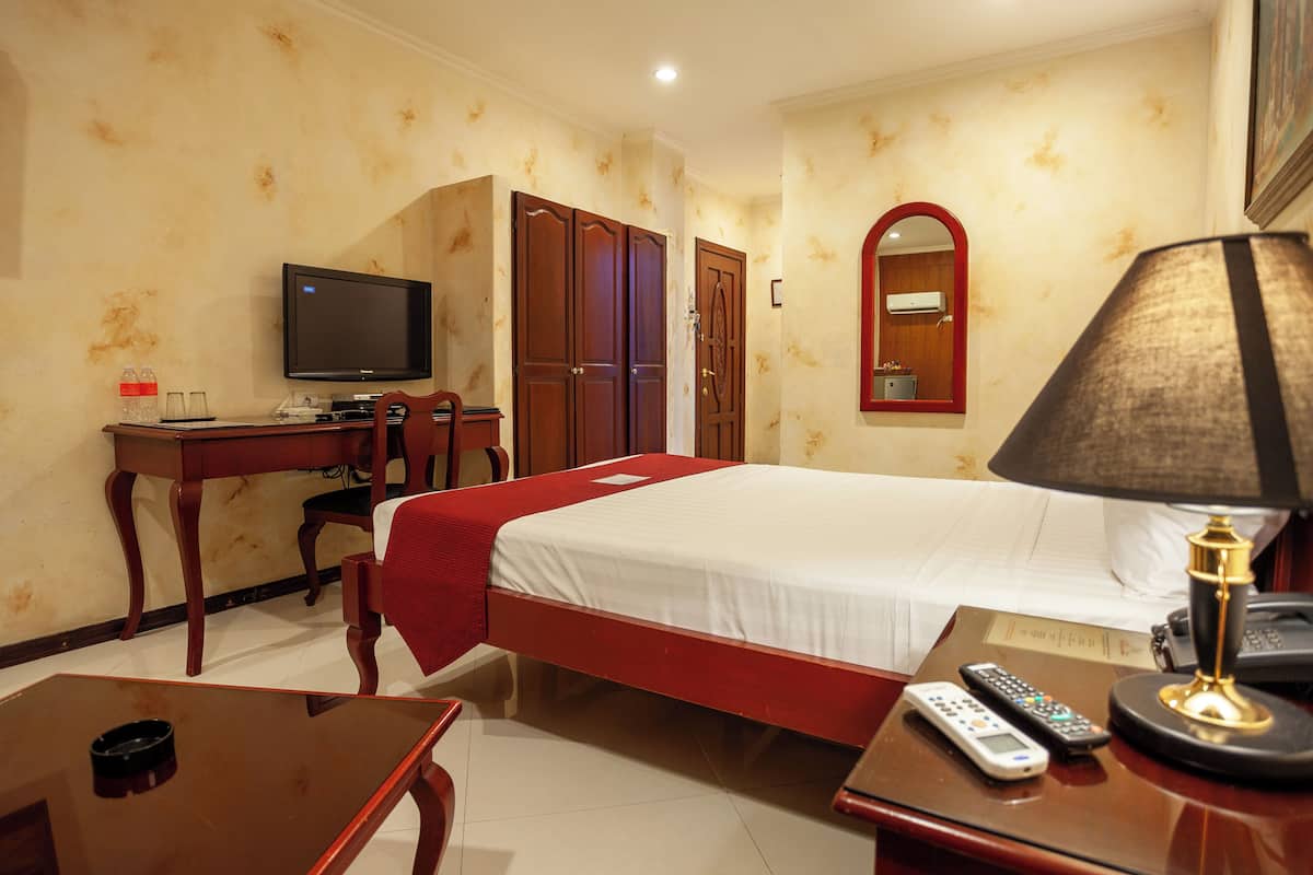 Une chambre d’hôtel comprenant un lit, un bureau avec une télévision, un miroir, une lampe et une télécommande.