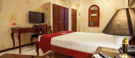 A hotel room with a bed, a desk with a television, a mirror, a lamp, and a remote control.