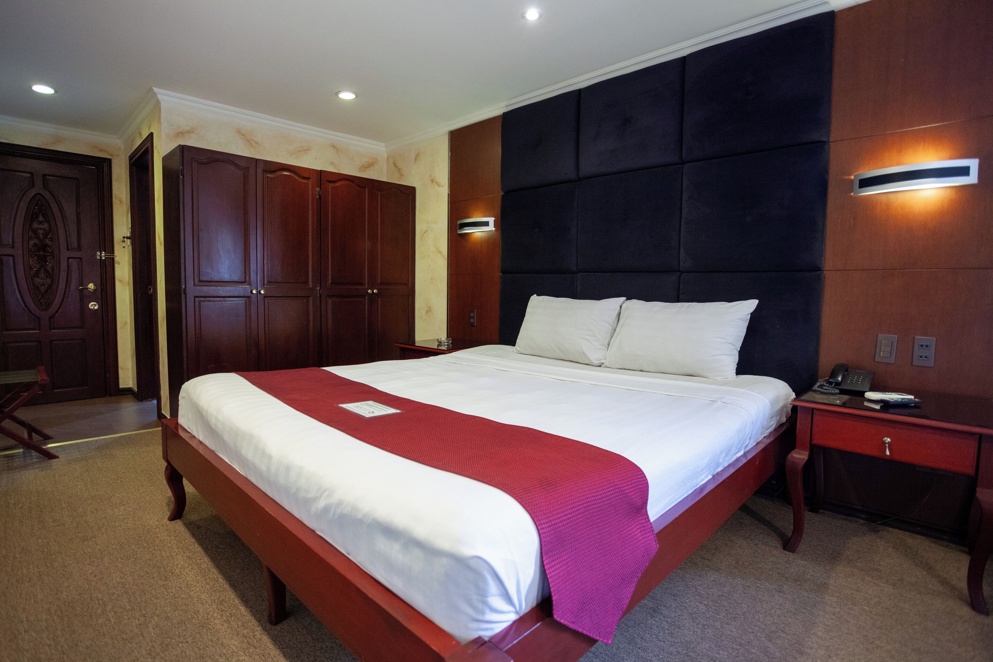 A hotel room with a large bed, wooden wardrobe, and a bedside table with a phone.