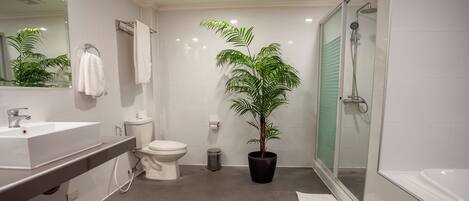 A modern bathroom with a sink, toilet, shower, and a potted plant.