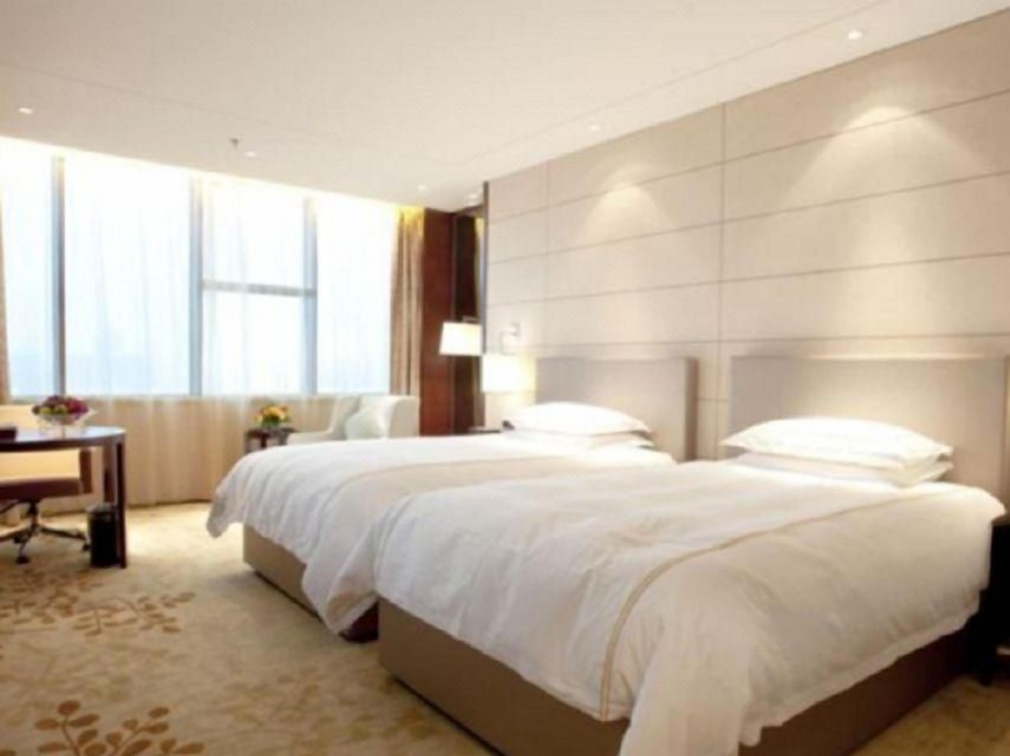 Una habitación de hotel con dos camas, un escritorio y un ventanal grande.