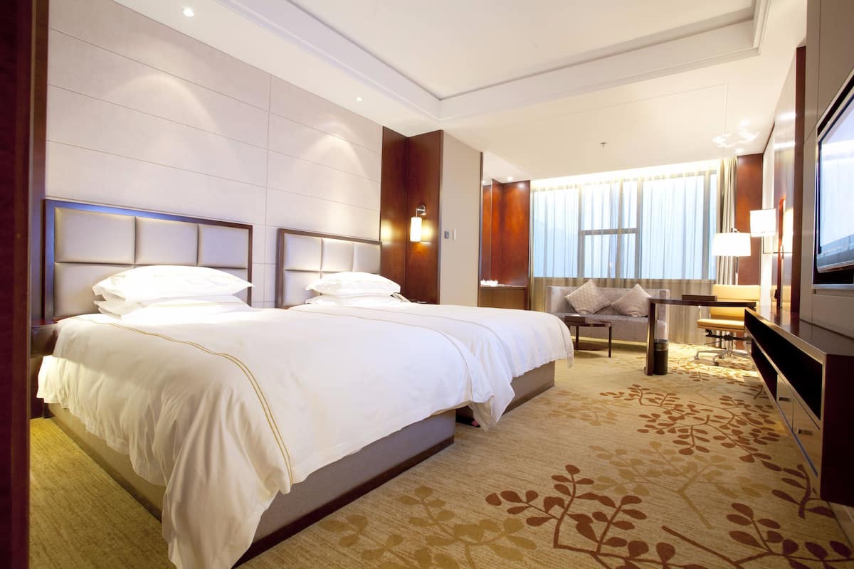 A hotel room with a large bed, a desk with a chair, a TV, and a window with curtains.