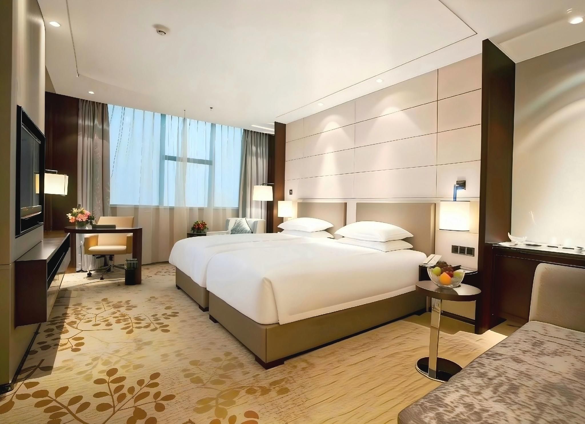 Ein Hotelzimmer mit einem großen Bett, einem Schreibtisch, einem Fernseher und einem Fenster mit Vorhängen.