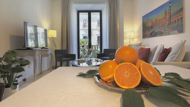 A hotel room with a bed, a dining table with fruit, a TV, and a balcony with a view. - NEW Luxurious Epicenter II Apartment:Free parking, Top location,Free A/C & Wi-Fi (Sevilla)