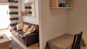 Ein Wohnzimmer mit braunem Ledersofa, gestreifteren Vorhängen, einem Spiegel und einem kleinen Tisch mit einem Glasbehälter.