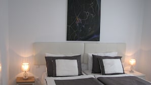 Ein Doppelbett mit weißem und dunkel gefärbtem Kopfteil, zwei Nachttische mit Lampen, ein kleiner Holznachttisch und ein an der Wand hängendes abstraktes Gemälde.