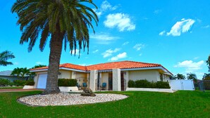 A two-story house with a red-tiled roof, a palm tree in the front yard, and a clear blue sky.